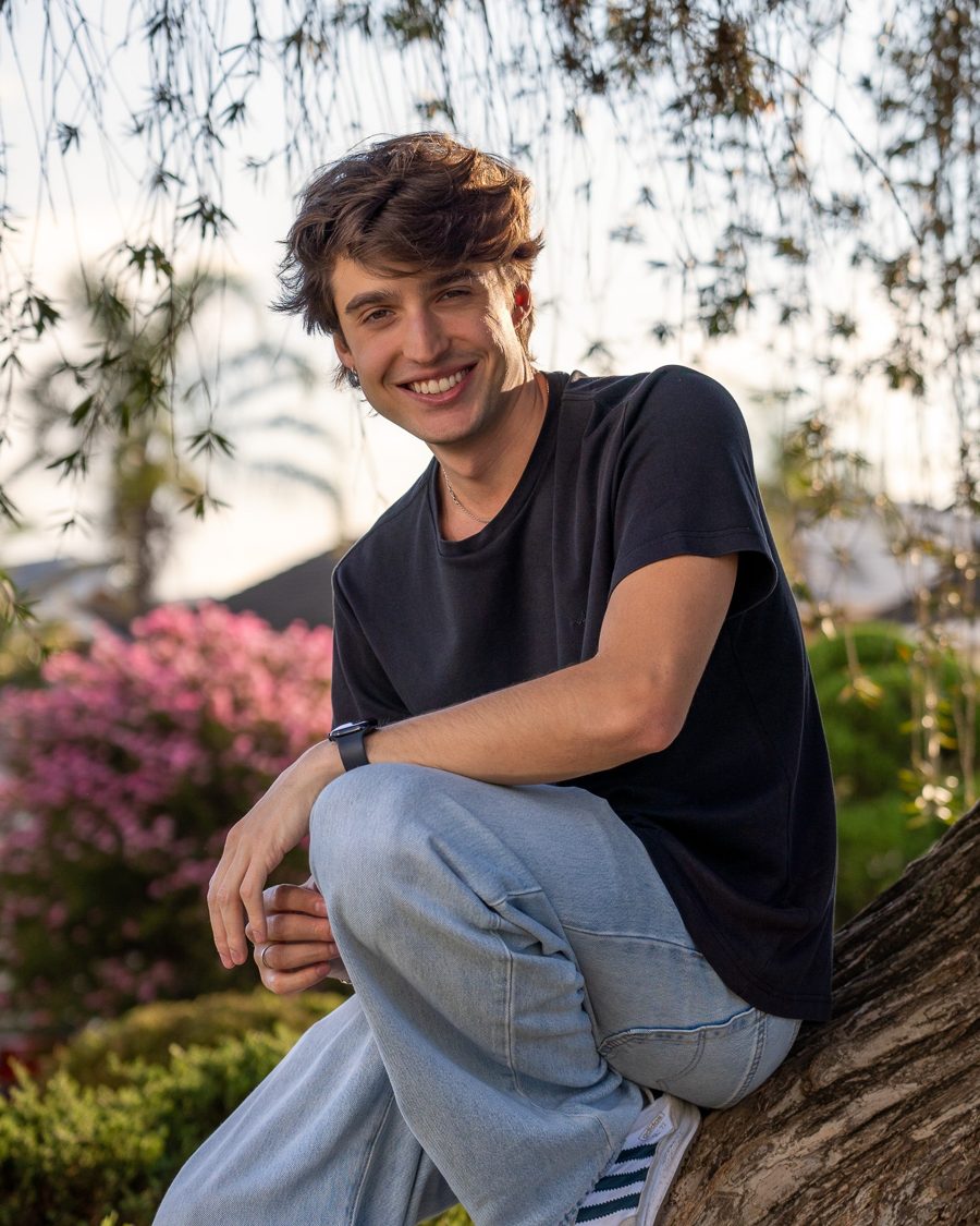Miguel Plaça sorrindo, sentado em uma árvore